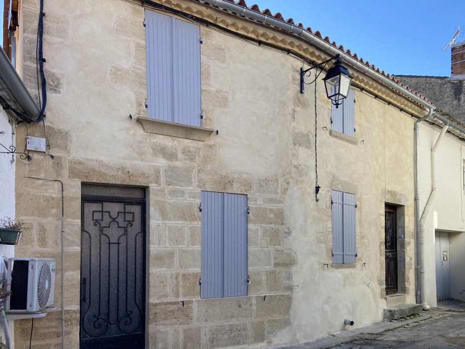 Façade de maison traditionnelle en pierre calcaire avec volets bleus fermés, porte d'entrée ornée de ferronnerie décorative