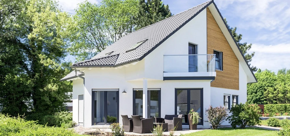 Jardin résidentiel en automne avec portail en pierre naturelle ouvert, pelouse partiellement dégradée, arbre à feuillage jaune doré au centre, haies taillées et cyprès
